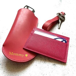 Puede incluir: Un conjunto de tres accesorios de cuero rosa: una funda para gafas con la palabra "Mommy" y un coraz&oacute;n, un porta tarjetas y un llavero.