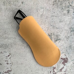 Puede incluir: Un estuche para gafas de cuero amarillo con un par de gafas negras en su interior.