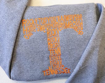 Może przedstawiać: Szara bluza z haftowanym pomarańczowym tekstem, który brzmi "Rocky Top You'll Always Be Home Sweet Home To Me Good Ole Rocky Top Tenn Essee Rocky Top Tennessee".