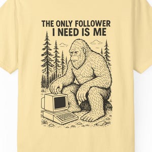 May include: Light yellow t-shirt with a black graphic of a Bigfoot sitting in front of a computer. The text "THE ONLY FOLLOWER I NEED IS ME" is above the graphic. The shirt is made of a soft material.