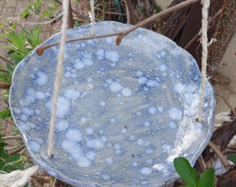 Op de afbeelding: Een blauwe keramische hangpot met een witte en gele gespikkelde glazuur. De pot wordt opgehangen met twee witte koorden.
