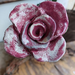 Pode incluir: Uma rosa de cerâmica com uma cor bordô profunda e detalhes brancos. A rosa é feita para parecer uma rosa real com várias camadas de pétalas.