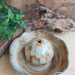 May include: A ceramic incense burner with a light blue and brown glaze. The burner has a round, hollow top and a wide, scalloped base.