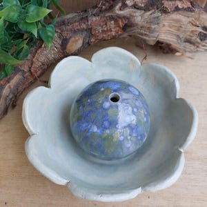 May include: A blue and green ceramic incense burner with a flower-shaped base. The burner has a small hole in the top for incense sticks.
