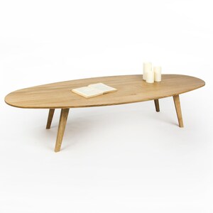 May include: A light wood oval coffee table with four legs. A book and three candles are on the table.
