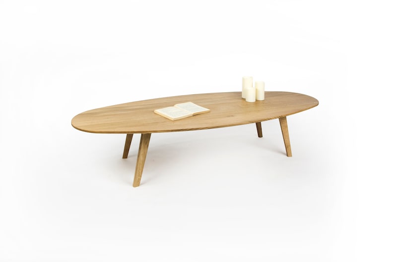 May include: A light wood oval coffee table with four legs. A book and three candles are on the table.