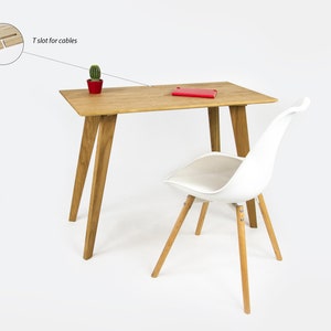 Könnte beinhalten: Ein heller Holzschreibtisch mit einem weißen Stuhl. Der Schreibtisch hat einen T-Schlitz für Kabel und einen kleinen Topf mit einem Kaktus auf der Oberfläche. Ein rotes Notizbuch liegt auf dem Schreibtisch.