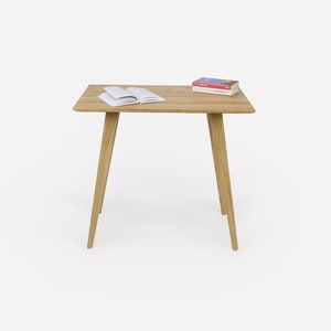 Może przedstawiać: Jasny drewniany stolik z prostokątnym blatem i czterema nogami. Na stole leżą dwie książki.