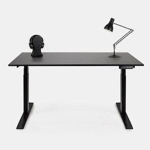 Peut inclure: Un bureau debout noir avec une lampe de bureau noire et un casque noir sur un support. Le bureau a un panneau de commande noir sous le plateau du bureau.
