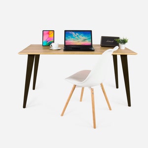 Pode incluir: Uma mesa de madeira com pernas de metal preto, uma cadeira branca com pernas de madeira, um computador portátil, um tablet, uma xícara de café e uma pequena planta em vaso. A mesa está colocada sobre um fundo branco.