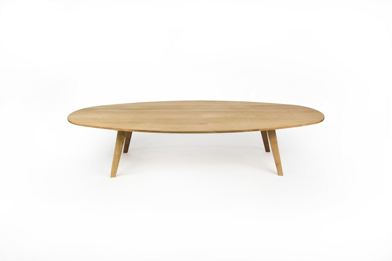 May include: A light wood oval coffee table with four tapered legs.