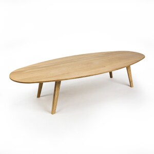 May include: A light wood oval coffee table with four legs. The table is on a white background.