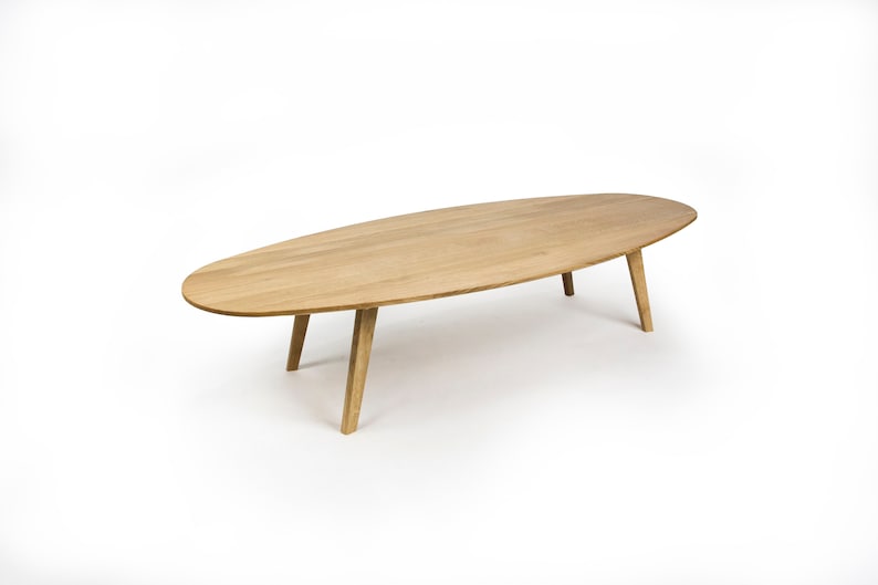 May include: A light wood oval coffee table with four legs. The table is on a white background.