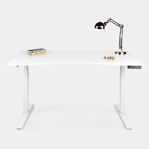 Peut inclure: Un bureau debout blanc avec un panneau de commande noir sur le côté droit. Le bureau a un plateau blanc et des pieds blancs. Il y a quelques petits objets sur le bureau, dont une pile de livres et une lampe de bureau.
