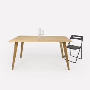 Puede incluir: Una mesa de comedor de madera clara con una tapa rectangular y cuatro patas anguladas. Una silla plegable negra está a la derecha de la mesa.