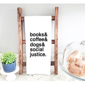 May include: White kitchen towel with black text that reads "books & coffee & dogs & social justice."