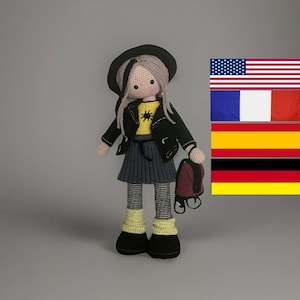Könnte beinhalten: Handgefertigte Häkelpuppe mit schwarzer Jacke, grauem Rock und schwarzem Hut. Die Puppe hat graues Haar und hält einen kleinen roten Rucksack. Das gelbe Shirt der Puppe hat eine schwarze Grafik. Die Puppe trägt schwarze Schuhe und gestreifte Socken.
