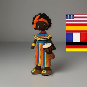 Könnte beinhalten: Handgefertigte Häkelpuppe mit dunkler Haut, die ein blau-orange gestreiftes Kleid, ein gelb-blaues Oberteil und braune Schuhe trägt. Die Puppe hat schwarzes Haar mit einem orangefarbenen Stirnband und hält eine kleine Trommel.