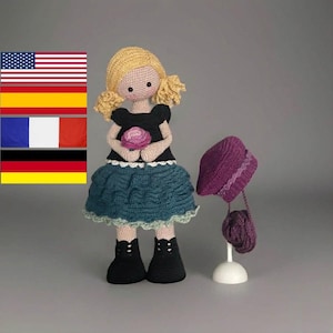 Könnte beinhalten: Handgefertigte Häkelpuppe mit blonden Zöpfen, trägt ein schwarzes Oberteil, einen türkisfarbenen Rock und schwarze Stiefel. Ein lila Hut und eine Handtasche werden auf einem weißen Ständer ausgestellt. Die Puppe hält eine rosa Blume.