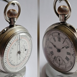 May include: A silver pocket watch with a white face and black Roman numerals. The watch has a small seconds dial and a silver case. The watch is displayed on a silver stand. The watch has a gold-coloured crown.