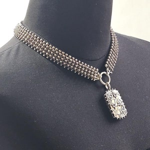 Può includere: Un girocollo in argento con un ciondolo a medaglione in argento. Il medaglione ha un design floreale.