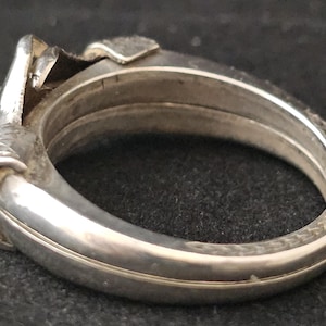 May include: A silver-toned hinged bangle bracelet. The bracelet has a detailed design on the clasp and decorative elements. The bracelet is made of metal and has a polished finish. The bracelet is a jewelry item.