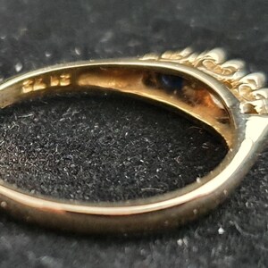 K&ouml;nnte beinhalten: Ein Goldring mit einem blauen Edelstein und kleinen klaren Edelsteinen auf der Ringschiene. Die Innenseite der Schiene ist mit "375" gekennzeichnet.