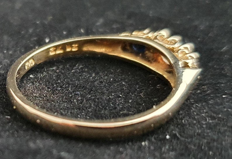 K&ouml;nnte beinhalten: Ein Goldring mit einem blauen Edelstein und kleinen klaren Edelsteinen auf der Ringschiene. Die Innenseite der Schiene ist mit "375" gekennzeichnet.