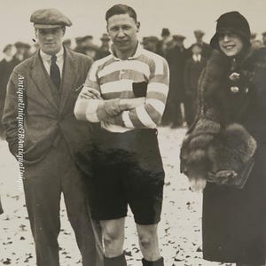 May include: A monochrome photograph featuring three individuals. A man in a striped rugby shirt stands with crossed arms. Two others are formally dressed, one in a tweed cap and the other in a fur stole.