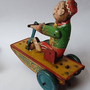 Può includere: Una scimmia di latta giocattolo vintage che indossa un cappello rosso e bianco, in sella a una motocicletta giocattolo gialla e rossa con ruote blu.