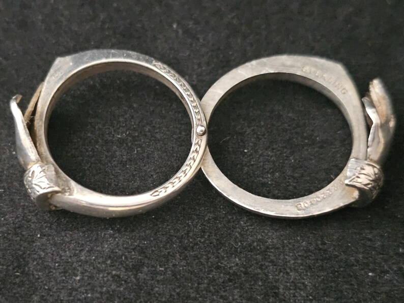 May include: A silver-toned bracelet with two connected circular bands. Each band features a hand-shaped clasp and decorative detailing. The bracelet is displayed on a dark surface.