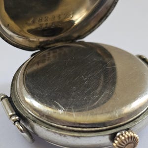 Op de afbeelding: Zilveren zakhorloge met een scharnierende achterkant. De achterkant is open en onthult het innerlijk van het horloge. De achterkant van het horloge is gegraveerd met het nummer 4823472 en 5163.
