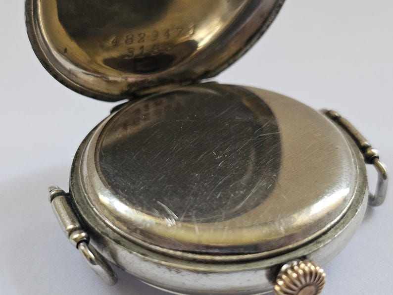 Op de afbeelding: Zilveren zakhorloge met een scharnierende achterkant. De achterkant is open en onthult het innerlijk van het horloge. De achterkant van het horloge is gegraveerd met het nummer 4823472 en 5163.
