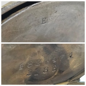 Op de afbeelding: Close-up van de achterkant van een zilveren zakhorloge met de nummers 4829471 en 3183 gegraveerd in het metaal. De letter E is gegraveerd op de bovenkant van het horloge.