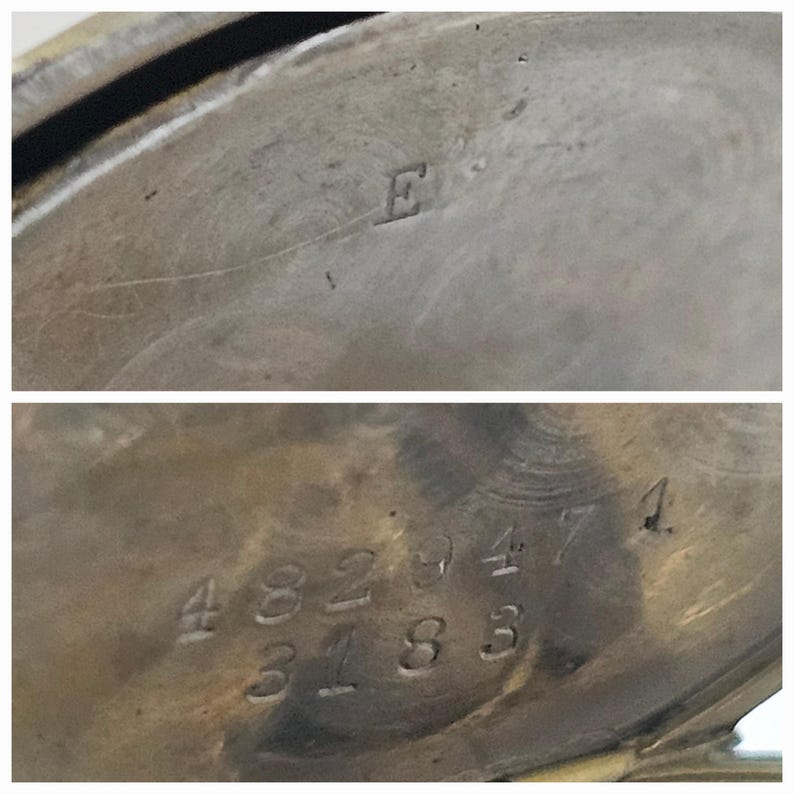 Op de afbeelding: Close-up van de achterkant van een zilveren zakhorloge met de nummers 4829471 en 3183 gegraveerd in het metaal. De letter E is gegraveerd op de bovenkant van het horloge.
