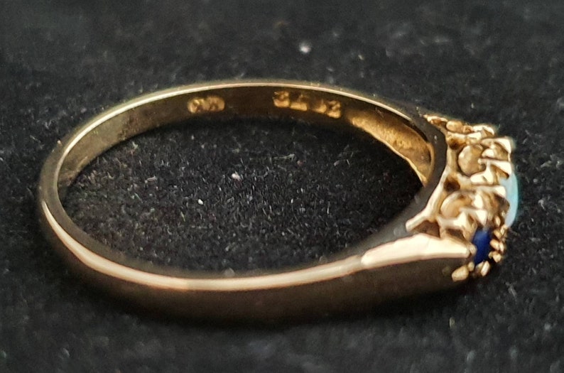 K&ouml;nnte beinhalten: Ein goldener Ring mit einem blauen und wei&szlig;en Opal-Stein und kleineren blauen Steinen, die in einem floralen Design eingefasst sind. Der Ring ist innen mit "375" gekennzeichnet.