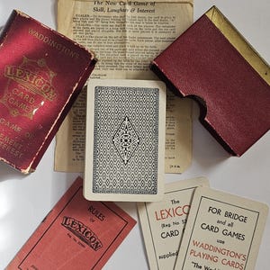 Könnte beinhalten: Vintage Lexicon Kartenspiel-Set mit roter Box und Regelbuch. Das Set enthält Spielkarten mit einem Rautenmuster und dem Text "Waddington's Playing Cards". Das Spiel ist für Bridge und andere Kartenspiele.
