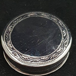 May include: A silver round trinket box with an intricate floral design around the edge.