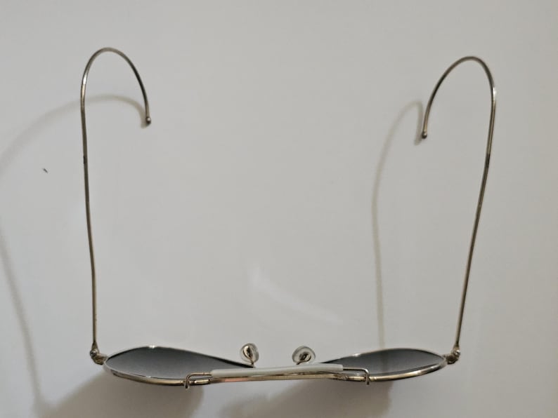 Pu&ograve; includere: Occhiali da sole con montatura argentata e lenti scure. Gli occhiali hanno un design classico con aste curve e un ponte. Le lenti sono di forma ovale e la montatura &egrave; di colore argento lucido. Su sfondo bianco.