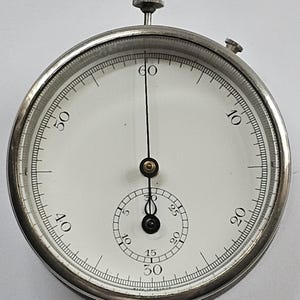 May include: A silver circular analogue timer with a black hand and a white face. The face has black numbers from 0 to 60 around the outer edge and smaller black numbers from 5 to 30 around the inner edge.