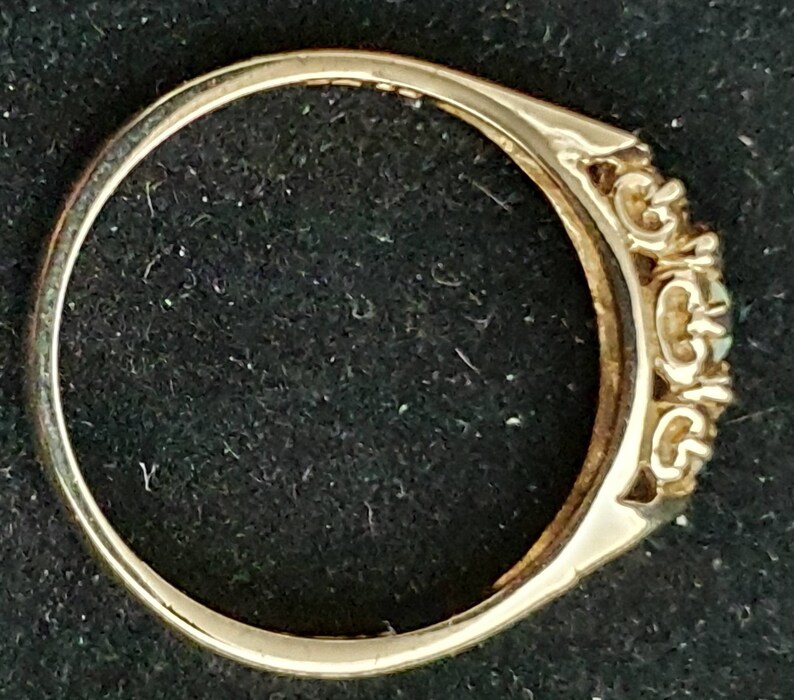 K&ouml;nnte beinhalten: Ein goldener Ring mit drei ovalen Edelsteinen, die in einem dekorativen Band gefasst sind.