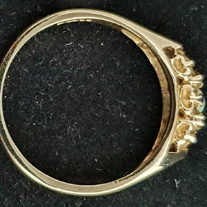 K&ouml;nnte beinhalten: Ein goldener Ring mit einer Reihe kleiner Diamanten und einem gr&ouml;&szlig;eren gr&uuml;nen Stein in der Mitte.