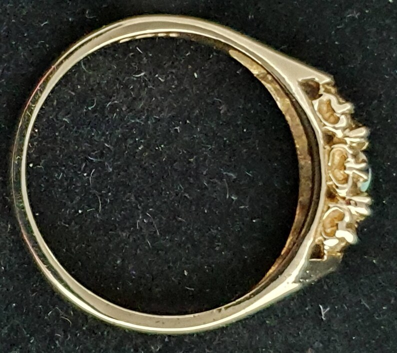 K&ouml;nnte beinhalten: Ein goldener Ring mit einer Reihe kleiner Diamanten und einem gr&ouml;&szlig;eren gr&uuml;nen Stein in der Mitte.