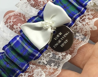 May include: Blue and green tartan garter with white lace and a white satin bow. A silver charm with the text "YOUR ENGRAVING HERE" is attached to the bow.