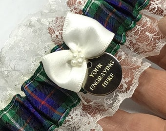 May include: White lace garter with a green, blue, and red plaid ribbon and a white satin bow. A silver charm with the text "YOUR ENGRAVING HERE" is attached to the bow.