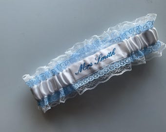 Embroidered personalised garter in white, bridal white or Ivory with a choice of embroidery thread colour. Trimmed in blue lace.