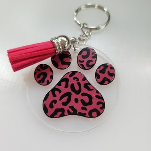 Pode incluir: Um chaveiro com a forma de uma pata de leopardo rosa e preta com um tassel rosa.