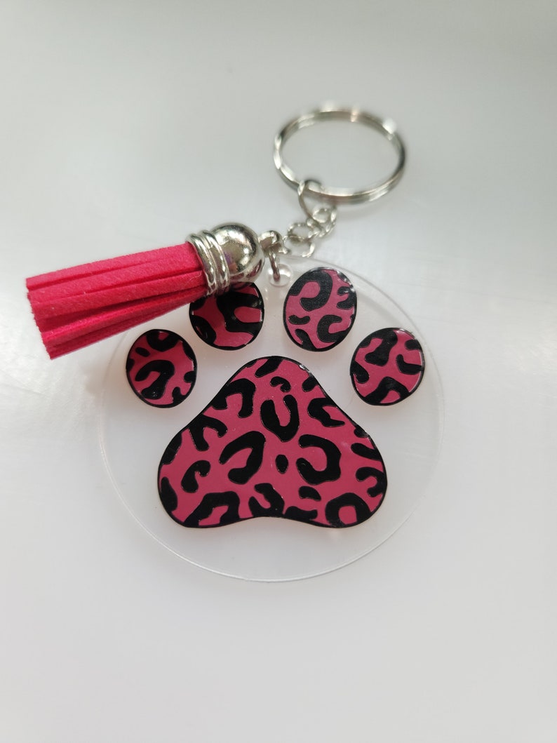 Pode incluir: Um chaveiro com a forma de uma pata de leopardo rosa e preta com um tassel rosa.