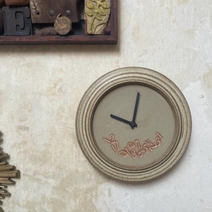 May include: A white ceramic clock with black hands and orange numbers. The clock has a raised rim and a textured surface.