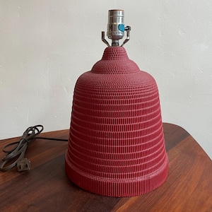 K&ouml;nnte beinhalten: Eine rote Keramik-Tischlampe mit einem strukturierten, glockenf&ouml;rmigen Schirm und einem silbernen Metallfu&szlig;.